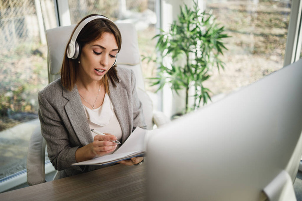 Eine nachdenkliche Geschäftsfrau sitzt mit Kopfhörern im Home Office und arbeitet online am Computer. - Foto, Bild