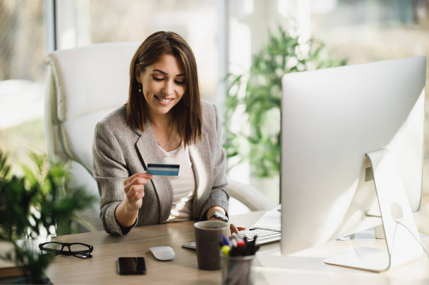 Usmívající se mladá obchodní žena dělá on-line bankovnictví na svém počítači v kanceláři. - Fotografie, Obrázek