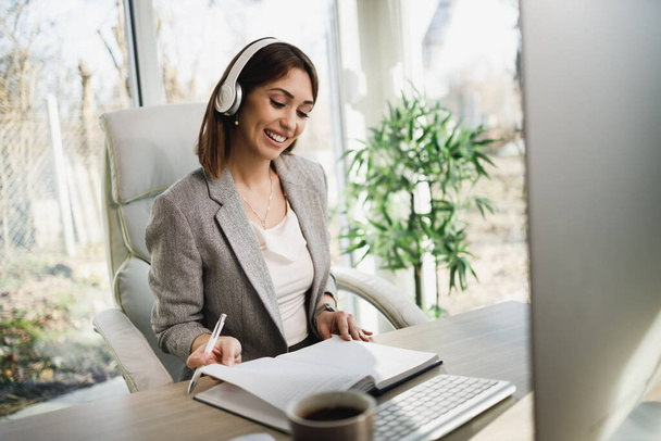 An attractive young woman with headphones working on computer at home office. - 写真・画像