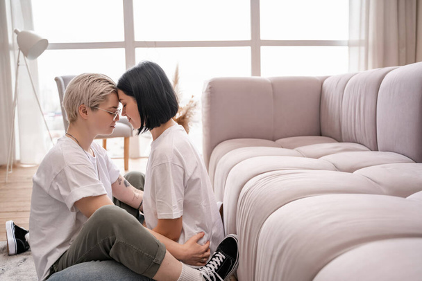 side view of cheerful lesbian couple with closed eyes in living room - Foto, imagen