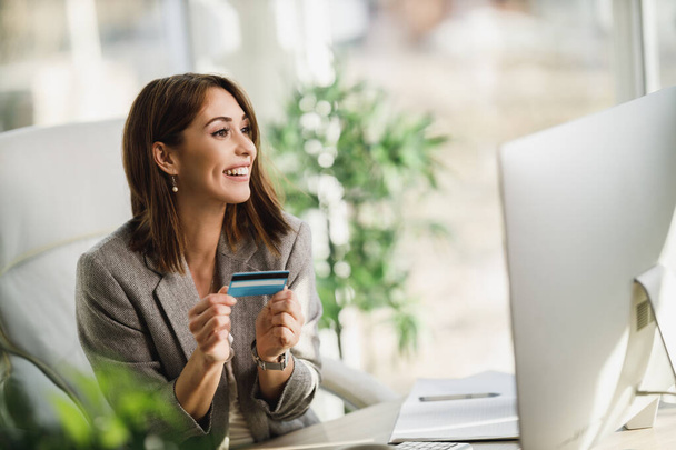 Una joven mujer de negocios sonriente usando una computadora y una tarjeta de crédito en la oficina. - Foto, Imagen