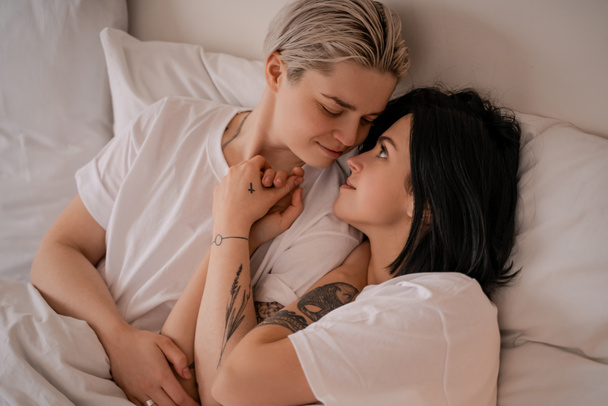 loving young lesbian couple lying in bed and holding hands - Фото, зображення