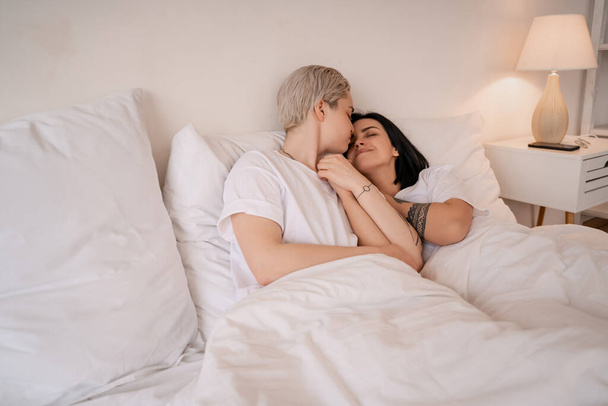 joven pareja lesbiana acostada en la cama, sonriendo y cogida de la mano - Foto, Imagen