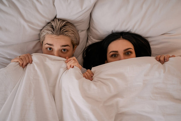 ブランケットの下のベッドに寝そべっている若いレズビアンカップルの  - 写真・画像