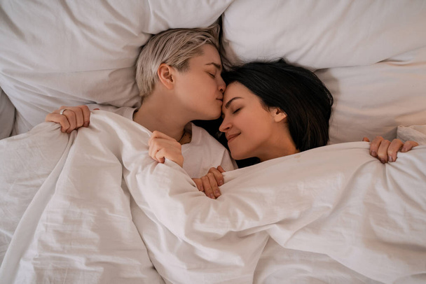 top view of lesbian couple lying in bed under blanket - Fotografie, Obrázek