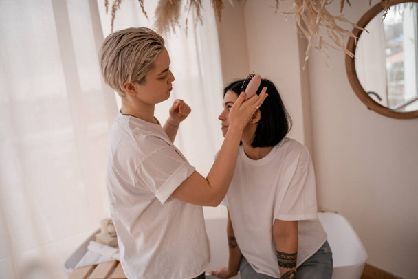 young woman brushing hair of brunette girlfriend in bedroom  - Fotoğraf, Görsel