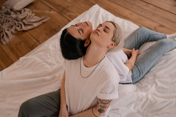 high angle view of lesbian couple sitting back to back on bed - Photo, Image