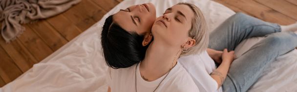 high angle view of lesbian couple sitting back to back on bed, banner - Photo, Image