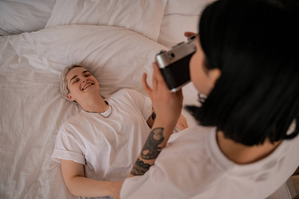 femme floue prenant une photo de petite amie allongée sur le lit et souriant sur la caméra rétro  - Photo, image