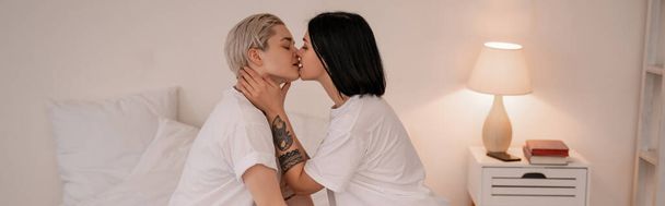 vista lateral de pareja lesbiana besándose en el dormitorio, pancarta - Foto, Imagen