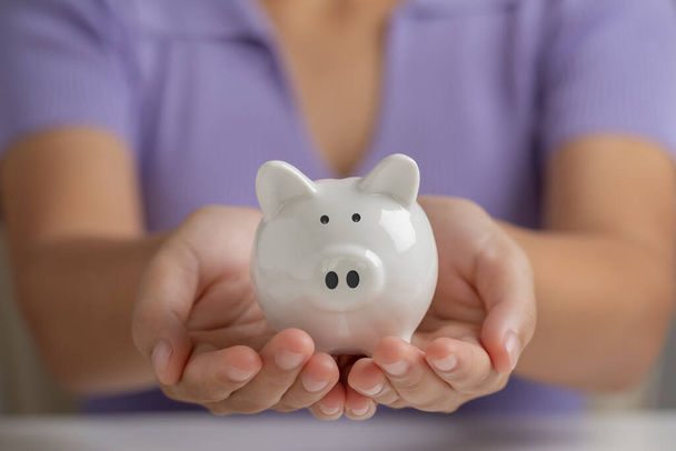 Mulher mão segurando branco porquinho banco, economizando dinheiro, depósito de dinheiro, conceito de finanças pessoais. - Foto, Imagem