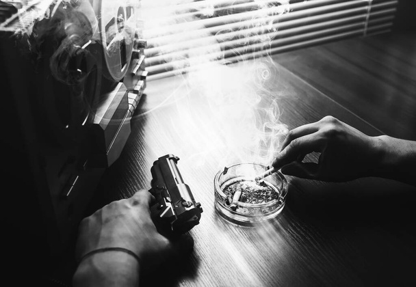 Special agent listens on the reel tape recorder. Officer is smoking a cigarette. KGB spying on conversations. Hand with cigarette near the ashtray. Gun on the table. - Photo, Image