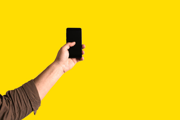 El hombre sostiene el teléfono inteligente en las manos sobre un fondo amarillo. Adicta a las tecnologías. - Foto, imagen