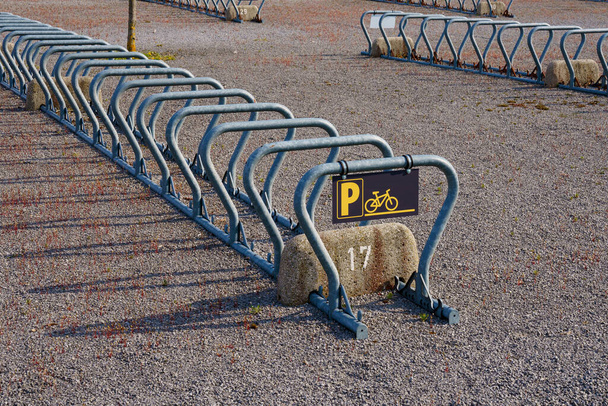 Pusty metalowy stojak na rowery przed stadionem. Czarno-żółta tabliczka. - Zdjęcie, obraz