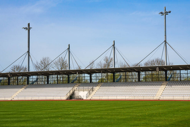 Üres állványok egy futballstadionból és egy zöld gyepből. Világító oszlopok a stadion felett. - Fotó, kép