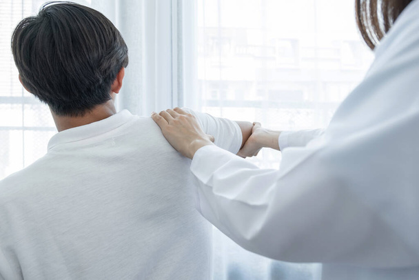 Vrouwelijke arts hand doet fysiotherapie door uitbreiding van de schouder van een mannelijke patiënt. - Foto, afbeelding