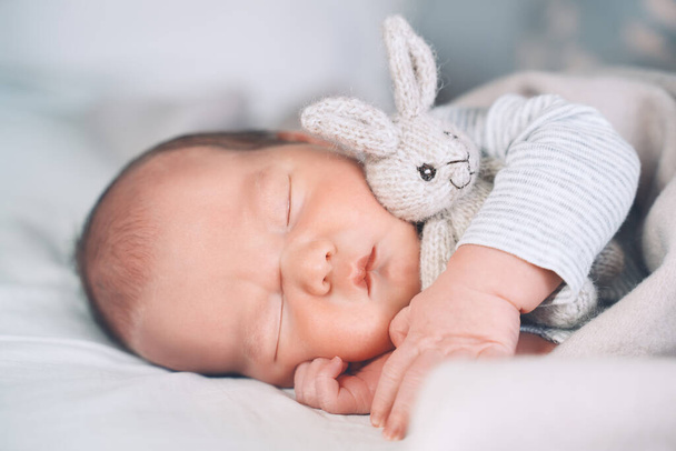 Newborn baby sleep at first days of life. Portrait of new born child boy one week old sleeping peacefully with a cute soft toy in crib in cloth background. - Fotó, kép