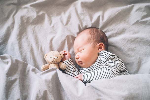 Newborn baby sleep at first days of life. Portrait of new born child boy one week old sleeping peacefully with a cute soft toy in crib in cloth background. - 写真・画像