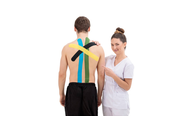 Giovane donna fisioterapista Applicando speciale nastro fisioterapico sulla schiena dell'uomo isolato su sfondo bianco - Foto, immagini