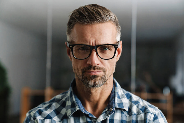 Ernsthafter weißhaariger Mann mit Brille blickt im Büro in die Kamera - Foto, Bild