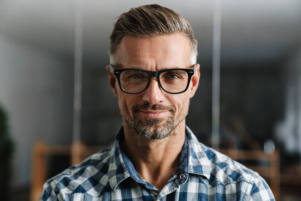 Pleased white-haired man in eyeglasses smiling at camera while standing in office - Foto, afbeelding
