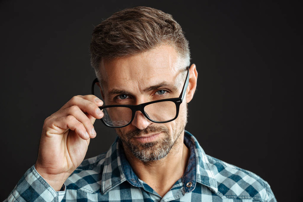 Handsome confident man in eyeglasses posing and looking at camera isolated over black background - Foto, immagini
