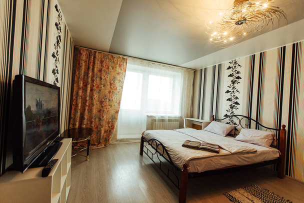 pościelone łóżko w mieszkaniu. podwójne przytulne łóżko. minimalistyczne wnętrze mieszkania w jasnych kolorach. miękka, czysta pościel w pokoju hotelowym. stolik nocny i krzesło - Zdjęcie, obraz