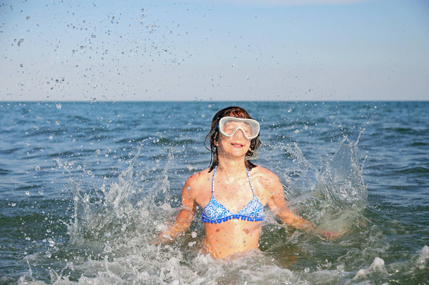 cute young caucasian girl plays in the sea water making splashes and jumps - Photo, Image