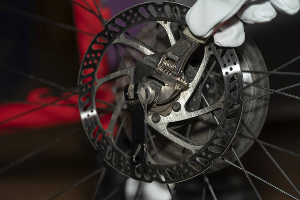 Remplacement de la roue arrière sur un vélo. Inspection technique du vélo. Démontage d'un véhicule à vélo avec une clé en gants de travail rouges - Photo, image