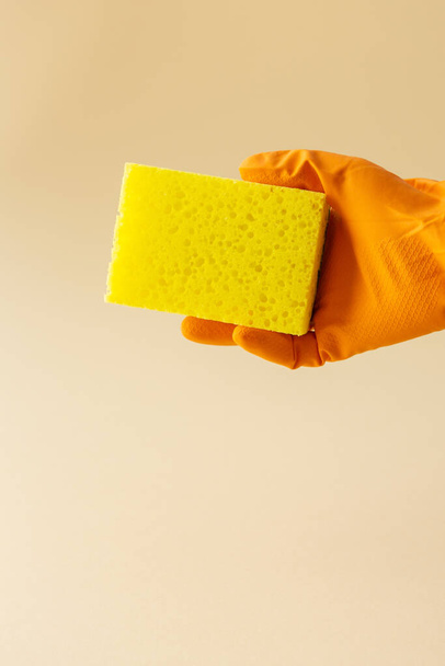 Main en gant de caoutchouc orange tient éponge de lave-vaisselle jaune, concept de nettoyage - Photo, image