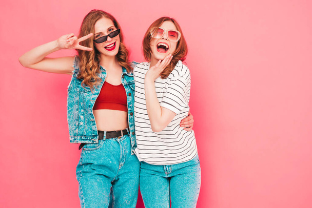 Two young beautiful smiling hipster female in trendy summer hipster  clothes. Sexy carefree women posing near pink wall in studio. Trendy and positive models having fun. Cheerful and happy - Zdjęcie, obraz