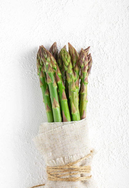 A bundle of a raw green asparagus in a linen cloth on white background, a bunch of a raw asparagus - Photo, image