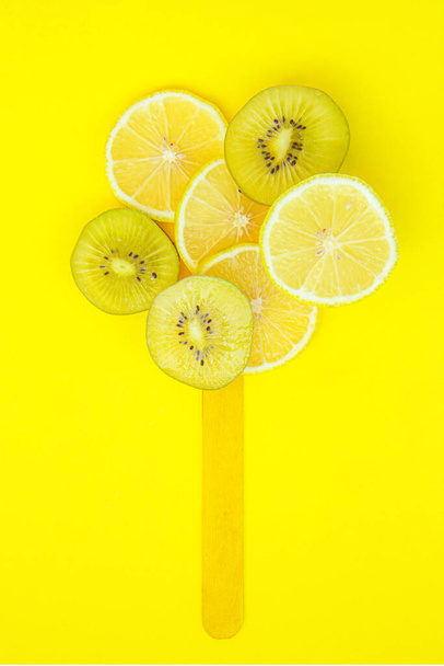 Concetto gelato alla frutta. Fette di limone e kiwi con bastoncino di gelato su fondo giallo brillante. Cibo concetto creativo. Estratto di frutta e verdura fresca. Vista dall'alto - Foto, immagini