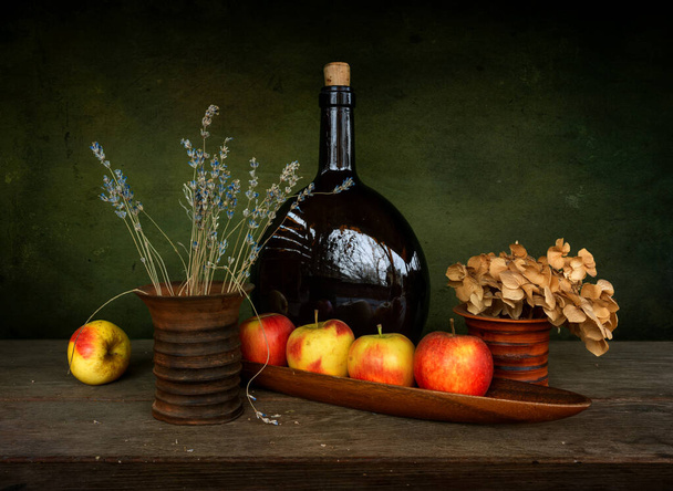 Still life with ripe apples, a large brown glass bottle and a bouquet of lavender in a ceramic vase. Vintage. - Foto, Bild