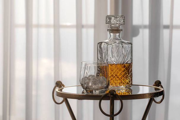 Decanter di vetro di whisky sala piena di liquore al whisky e due bicchieri con ghiaccio rocce su tavolo di vetro in accogliente interno dell'hotel - Foto, immagini