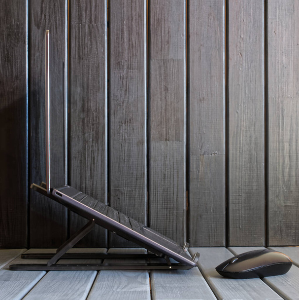 Um laptop prata moderno fino ou ultrabook montado em um suporte portátil dobrável contra um fundo de madeira. Painéis de pinheiro pintados. Estilo escandinavo. Vista lateral. Close-up - Foto, Imagem