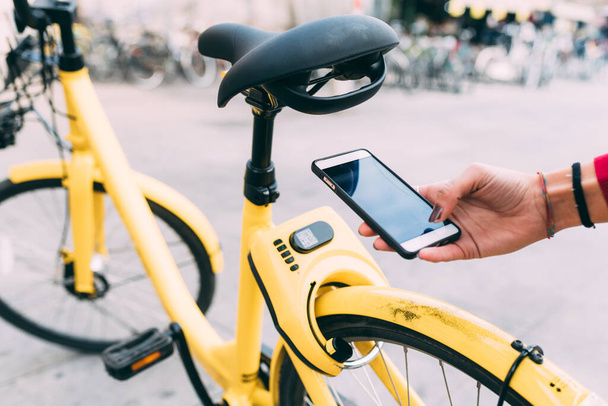 Cerca de la mano de la mujer usando el teléfono inteligente desbloqueo de bicicletas compartidas - Foto, imagen