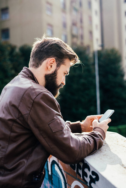 Молодой бородатый мужчина на открытом воздухе с помощью смартфона торговли в Интернете - Фото, изображение