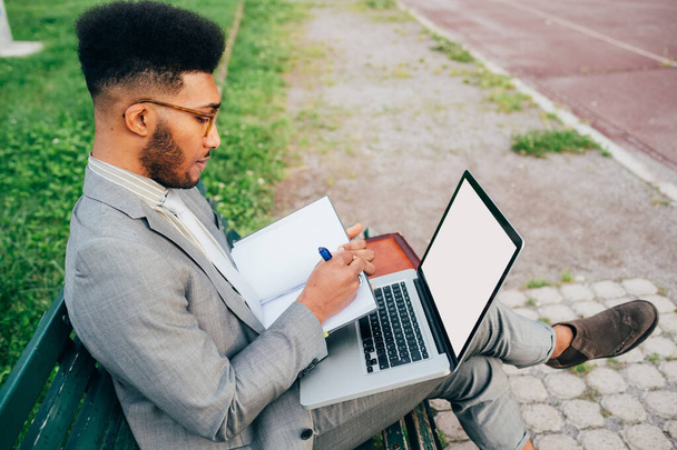 Jonge zwarte professionele zakenman op afstand werken met behulp van computer schrijven nota - Foto, afbeelding