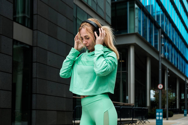 Attractive fit mature woman in green sport outfit enjoying music with headphones. Happiness. - Foto, immagini