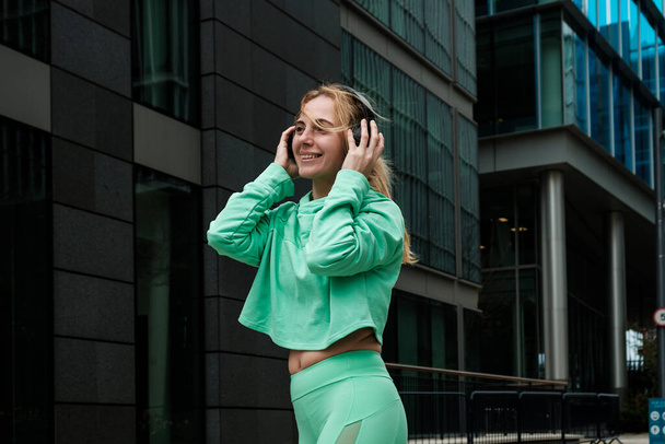 Aantrekkelijke pasvorm volwassen vrouw in groene sport outfit genieten van muziek met hoofdtelefoon. Geluk. - Foto, afbeelding