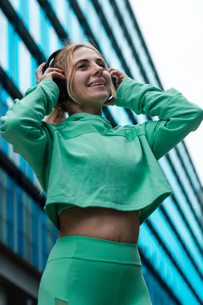 Ελκυστική ταιριάζει ώριμη γυναίκα φορώντας πράσινο ντύσιμο αθλητισμού απολαμβάνει τη μουσική με ακουστικά. - Φωτογραφία, εικόνα
