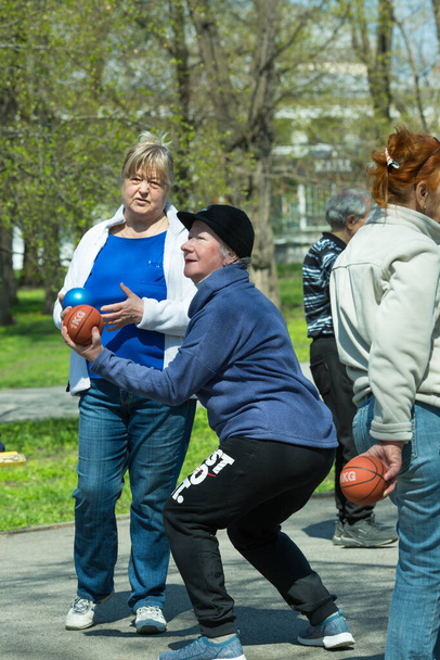 Dnepropetrovsk, Ουκρανία - 04.22.2021: Μια ομάδα ηλικιωμένων που κάνουν γυμναστική υγείας και φυσικής κατάστασης στο πάρκο. Οι γέροι κάνουν ασκήσεις με μπάλα.. - Φωτογραφία, εικόνα