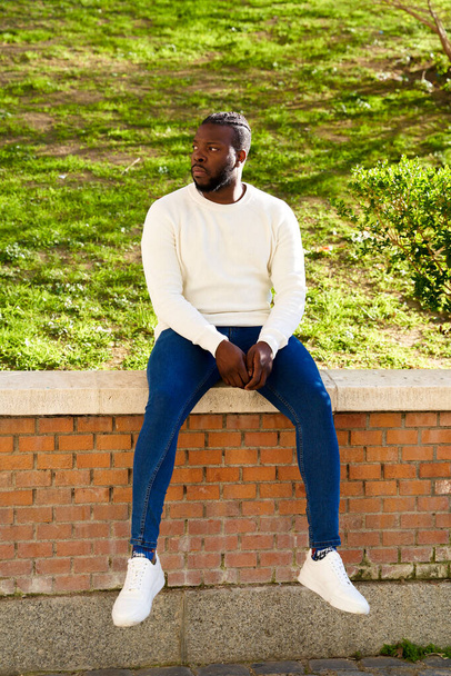 Young African American man sitting on a wall. Latino man walking through the city.  - Photo, Image