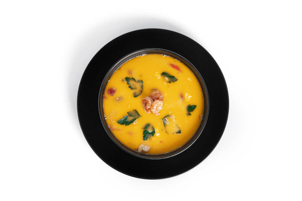 Soup with shrimps in a black deep dish isolated on a white background. Thai soup with seafood. Thai tom yum soup - Photo, Image