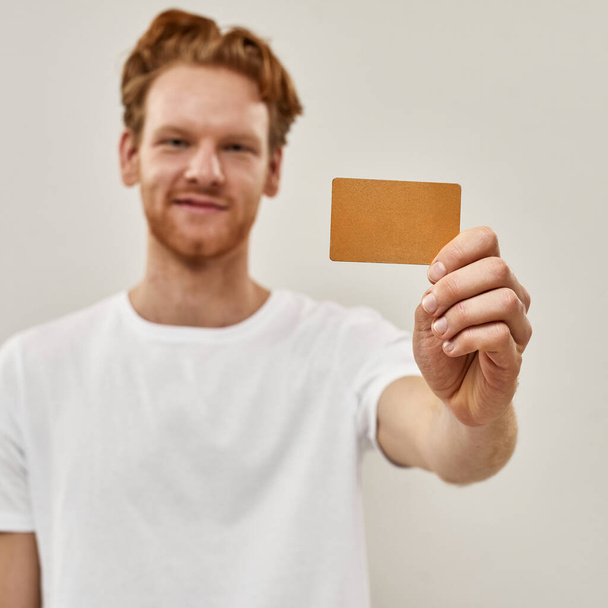 Young redhead man holds credit card in front of him - Fotografie, Obrázek