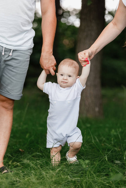 Onnellinen nuori perhe, äiti, isä ja poikavauva viettävät aikaa ulkona kesällä vihreässä puutarhassa. vanhemmat pitävät lastaan kädestä. - Valokuva, kuva