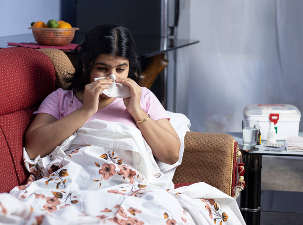 Hintli bir Asyalı kadın üşümüş ve kanepede yatarken peçete kullanmış. - Fotoğraf, Görsel