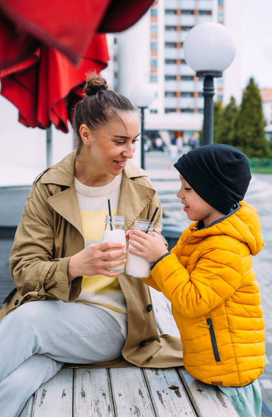 Young mom and son have fun and drink milkshake outdoors. - Photo, Image