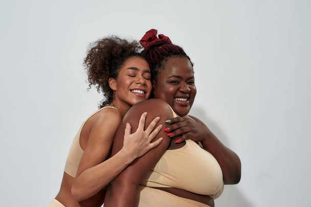 Two smiling african american women in underwear with different body size having fun, posing together isolated over gray background - Zdjęcie, obraz